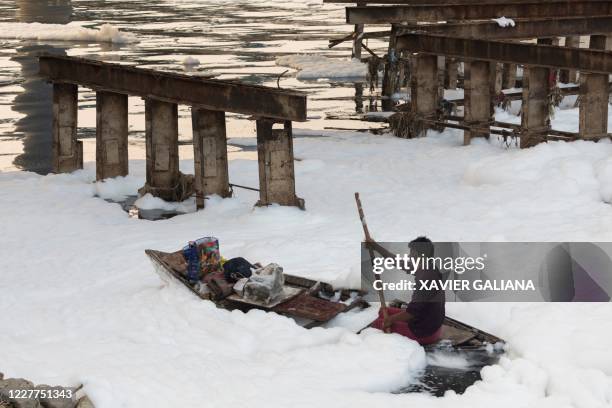 Man rows his boat amidst foam in the polluted Yamuna river on the outskirts of New Delhi on July 23, 2020.