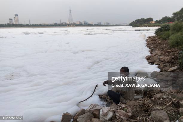 Fisherman pulls a fishing line amidst foam along the banks of the polluted Yamuna river on the outskirts of New Delhi on July 23, 2020.