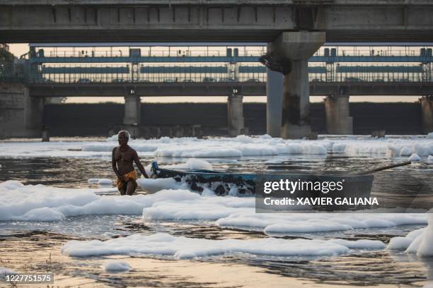 Man pulls a boat amidst foam in the polluted Yamuna river on the outskirts of New Delhi on July 23, 2020.