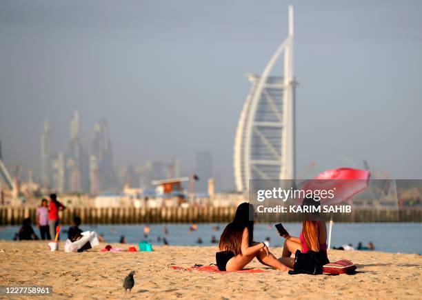 Woman sunbathers sit along a beach in the Gulf emirate of Dubai on July 24 while behind is seen the Burj al-Arab hotel. - After a painful four-month...