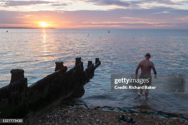 As the sun sets over fading daylight and calm waters of the Thames Estuary, a wild sea swimmer enters the water for his regular evening dip, on 18th...