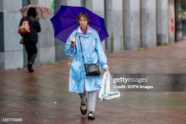 Woman seen wearing a raincoat and holding an umbrella during a rainy summer day. People wear protective masks on the shopping street of Rotterdam on...