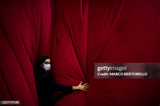 Theater worker wearing a protective face mask holds the curtain before a concert at the Arena in Verona, northern Italy, on July 25, 2020. - This is...