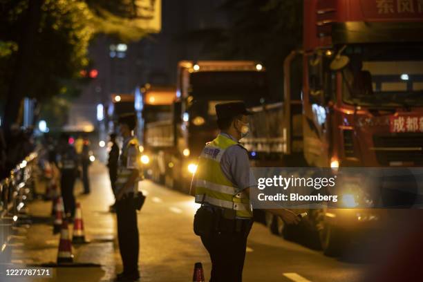 Police officers stand guard as large flatbed trucks pull up in front of the U.S. Consulate General Chengdu at night in Chengdu, China, on Sunday,...