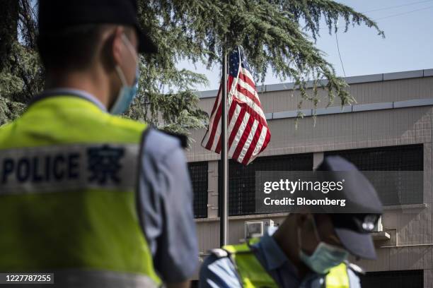 Police officers stand near an American flag flown in front of the U.S. Consulate General Chengdu in Chengdu, China, on Sunday, July 26, 2020....