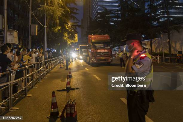 Police officers stand guard as large flatbed trucks pull up in front of the U.S. Consulate General Chengdu at night in Chengdu, China, on Sunday,...