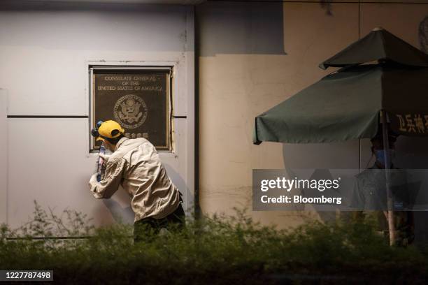 Worker tries to remove a plaque from the front of the U.S. Consulate General Chengdu at night in Chengdu, China, on Sunday, July 26, 2020....