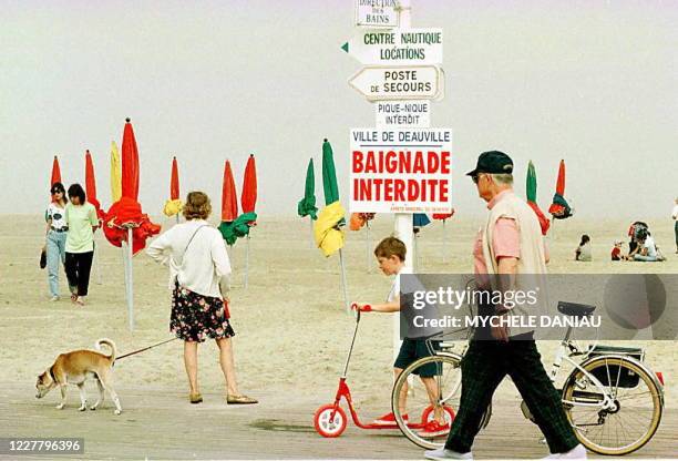 Des vacanciers passent devant la pancarte d'interdiction de baignade, le 09 août, sur la plage de Deauville suite aux hydrocarbures qui se sont...