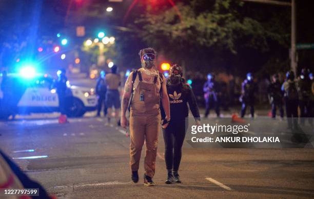 Couple hold hands as they walk on a street in Portland, Oregon early July 26 as protests continue across the United States following the death in...