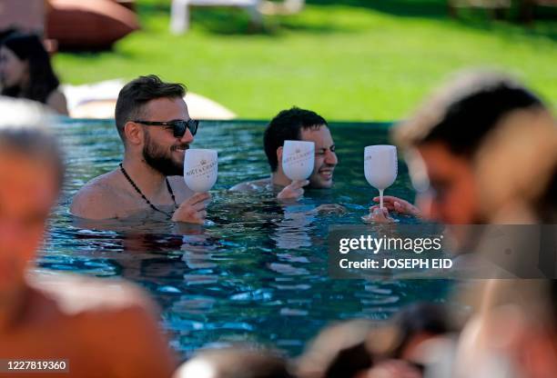 Lebanese people gather at a swimming pool in the upmarket Faqra Club in the Lebanese mountains north of Beirut on July 25, 2020. - Panama hats and...