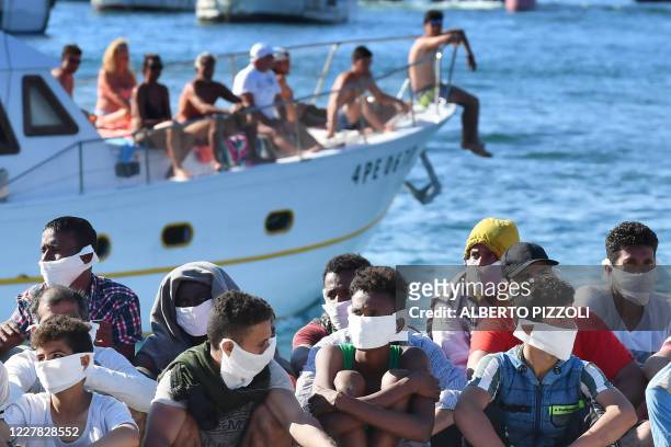 Migrants rescued by Italys' Guardia Costiera sits as a boat with tourists enter in the harbor of the Italian Pelagie Island of Lampedusa on July 29,...