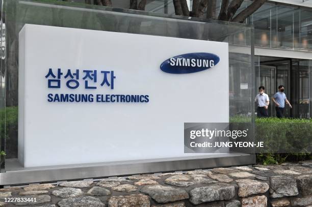 People walk past the logo of Samsung Electronics at the company's Seocho building in Seoul on July 30, 2020. - Samsung Electronics reported on July...