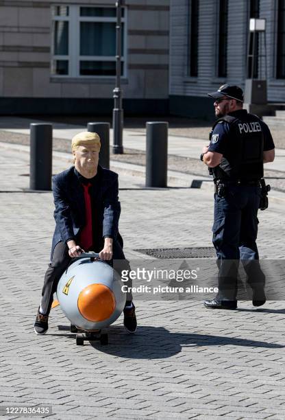 Policeman observes an activist dressed as US President Trump driving a mobile model of an atomic bomb in front of the Brandenburg Gate during a...