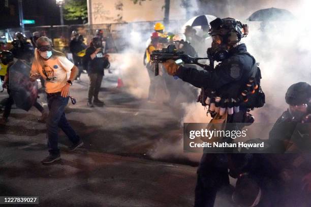 Federal officer points his less-lethal weapon into the crowd while dispersing a protest against racial injustice and police brutality in front of the...