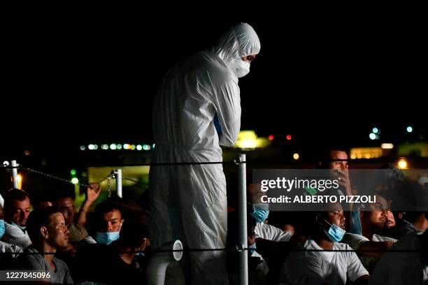 Migrants, wearing protective face mask, wait onboard an Italy's Guardia Costiera ship in the harbor of Italian Pelagie Island of Lampedusa, on July...