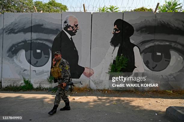 Security personnel walks past a wall mural with images of US Special Representative for Afghanistan Reconciliation Zalmay Khalilzad and Taliban...