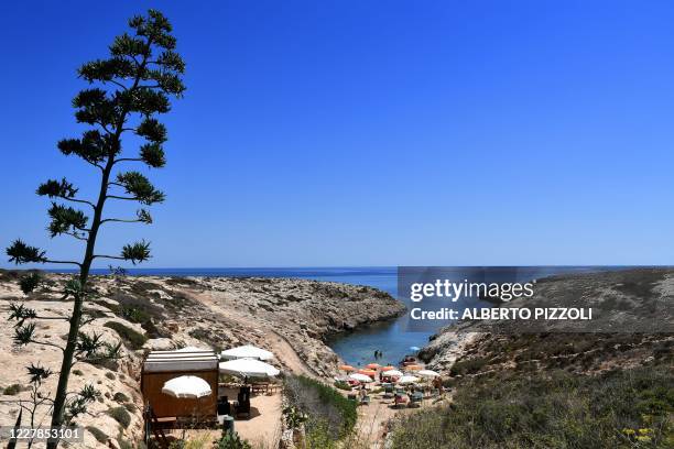 People sunbath and swim on a beach in the Italian Pelagie Island of Lampedusa on July 31, 2020. - Boats with migrants mainly from Tunisia continue to...