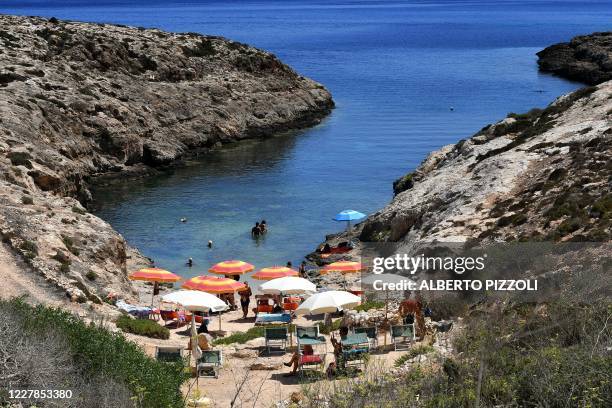 People sunbath and swim on a beach in the Italian Pelagie Island of Lampedusa on July 31, 2020. - Boats with migrants mainly from Tunisia continue to...