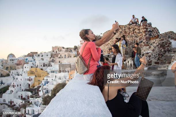 Tourists enjoying the amazing sunset at Oia in Santorini Volcano Island, in Cyclades, Aegean Sea, in Greece. They are gathered at a viewpoint on the...