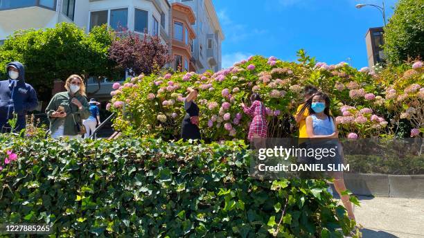 Tourists wearing masks take pictures on Lombard Street famous for a steep, one-block section with eight hairpin turns in San Francisco, California on...