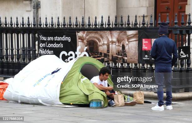 Man is seen standing infront of a homeless man sitting in a low quality tent near Trafalgar Square. London has seen a surge in rough sleepers as...