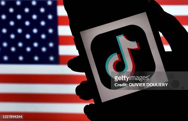 In this photo illustration, the social media application logo, TikTok is displayed on the screen of an iPhone on an American flag background on...