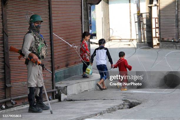 Kashmiri children cross the road bloack as Indian paramillitary trooper stands alert during strict restrictions in Srinagar, Indian Administered...