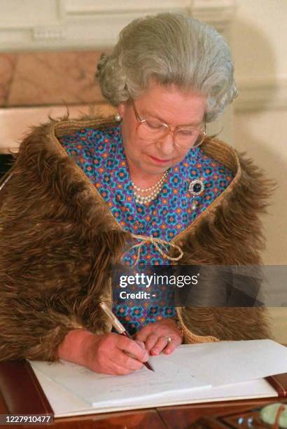 Queen Elizabeth II, wearing a traditional Maori cloak of Kiwi feathers, signs the final Tainui Settlement Bill at Government House in Wellington 03...