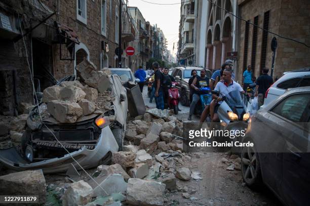 People ride past a car destroyed after a building wall collapsed after a large explosion on August 4, 2020 in Beirut, Lebanon. Video shared on social...
