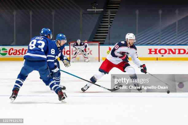 Alexander Wennberg of the Columbus Blue Jackets plays the puck against Ilya Mikheyev and Cody Ceci of the Toronto Maple Leafs during the first period...