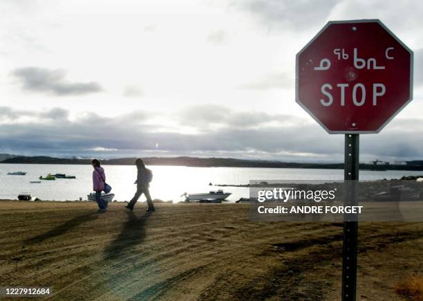 Two Inuit children return from school past a stop sign written in English and Inuit 02 October 2002 in Iqaluit, northern Canada. Iqaluit is the...