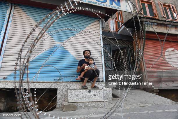 Man feeds his child next to barbed wire laid out during curfew at downtown area on August 4, 2020 in Srinagar, India. Curfew has been imposed in...