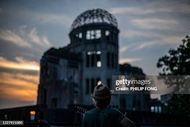 Man plays his guitar in front of in front of ruins of the Hiroshima Prefectural Industrial Promotion Hall, now commonly known as the atomic bomb...