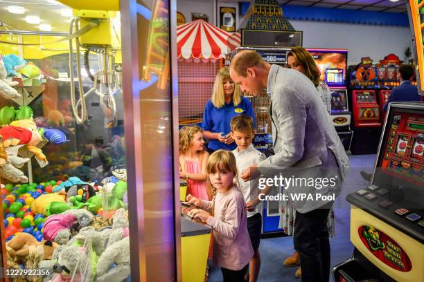 Prince William, Duke of Cambridge hands a coin to Jamie Case so he and his friend, Erin Phillips and sister Hollie Case can play on a grab a teddy...