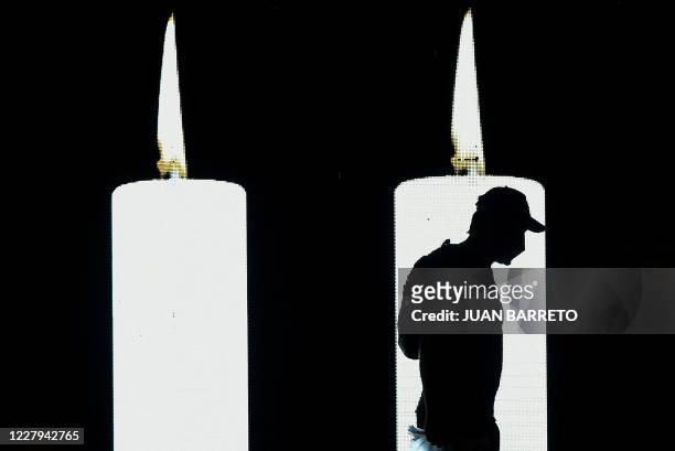 Man walks in front of a screen projecting candles in tribute to the dead by COVID-19 during the 482th anniversary of the city of Bogota, on August 6,...