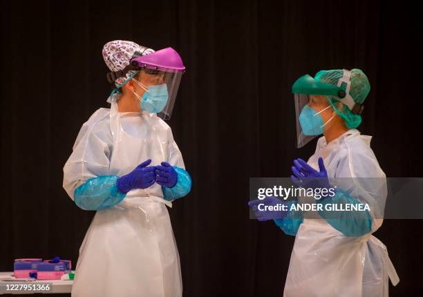 Healthcare workers talk as they wait for residents at a temporary testing center for the novel coronavirus in San Sebastian on August 7 following a...