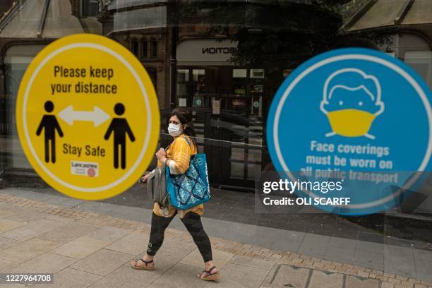 Woman walks past notices on a bus shelter advising people to maintain a social distance and wear face coverings, in the city centre of Preston, north...