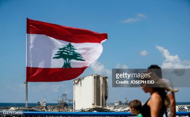 People walk along a bridge past a Lebanese flag flying near the port of Lebanon's capital Beirut on August 9 as in the background are seen the...