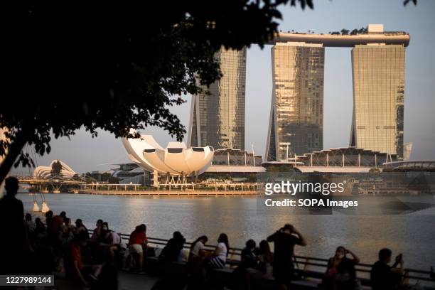 People wait by the Singapore River for fireworks with the Marina Bay Sands in the background during the Singapore National Day. Singapore celebrates...