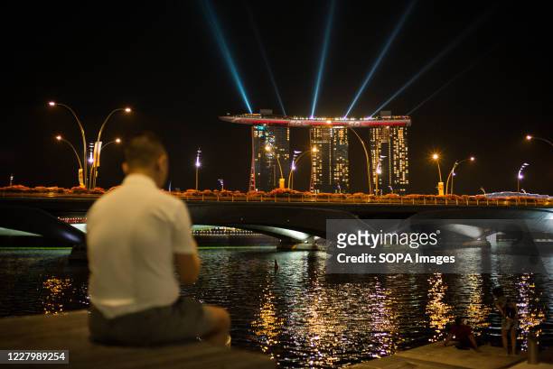 Man sits by the Singapore River, overlooking the Marina Bay Sands on the National Day. Singapore celebrates its 55th National Day on the 9th of...