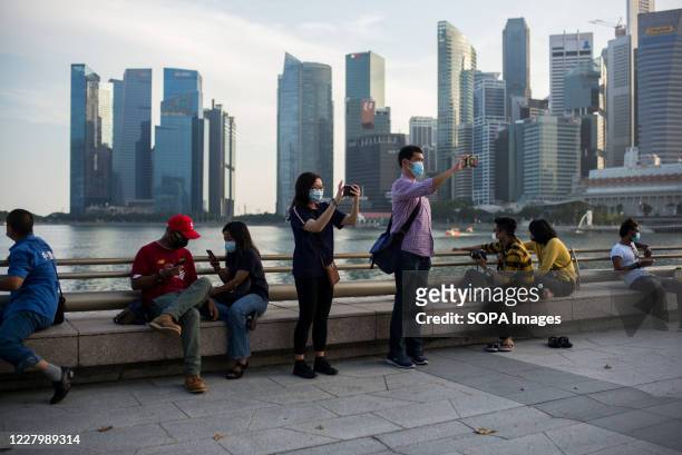 People wearing face masks as a preventive measure take pictures by the Singapore River, overlooking the central business district, during the...