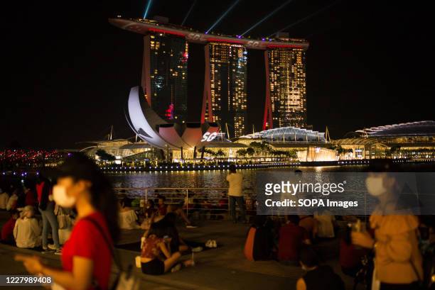People wearing face masks as a preventive measure waits by the Singapore River for the fireworks with the Marina Bay Sands in the background during...