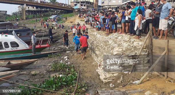 People observe from the shores of the Ucayali River as wounded and deceased are loaded onto barges in the remote town of Requena, hours away by boat...