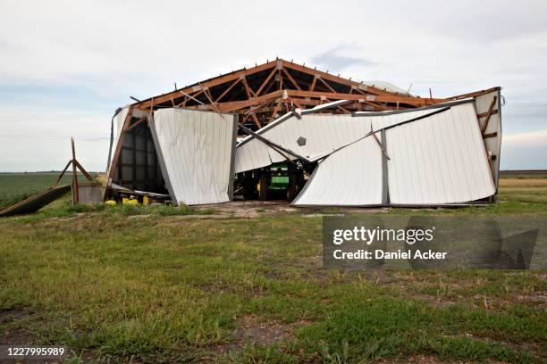 John Deere agricultural tractor sits under a collapsed building following a derecho storm, a widespread wind storm associated with a band of rapidly...