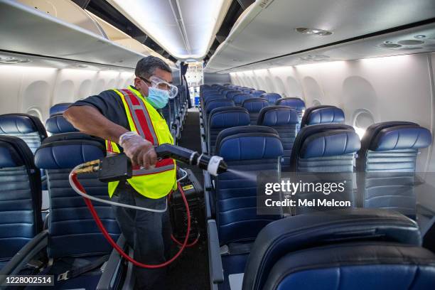 Cleaning supervisor Jose Mendoza uses an electrostatic sprayer to disinfect the cabin area of a United Airlines 737 jet before passengers are allowed...