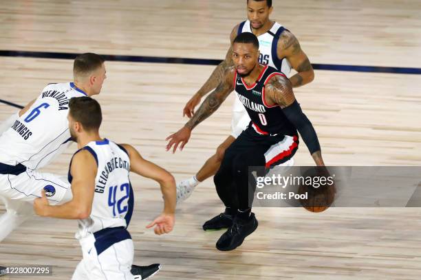 Damian Lillard of the Portland Trail Blazers controls the ball against Kristaps Porzingis and Trey Burke of the Dallas Mavericks during the first...