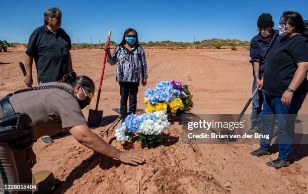 Carlita Bergen, center, holds a shovel as Navajo Nation police officer Carolyn Tallsalt smooths dirt over COVID-19 victim Arnold Billy's grave while...