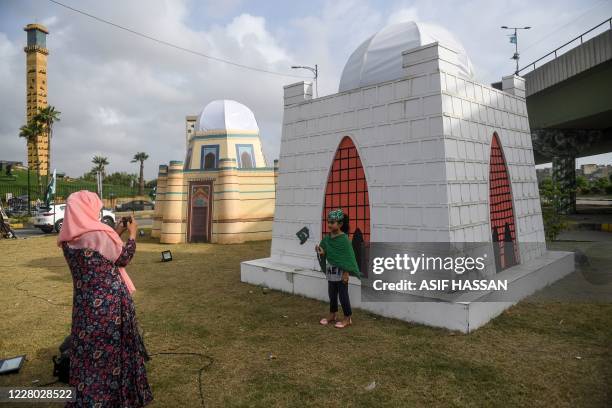 Woman takes a photograph of her daughter beside a model of the tomb of Mohammad Ali Jinnah, the founder of Pakistan, alongside a street in Karachi on...