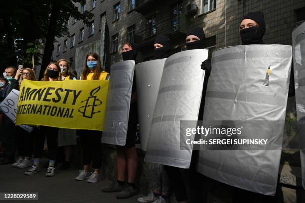 Activists dressed like riot policemen stand in line past Amnesty International activists as they and members of the Belarus diaspora take part in a...