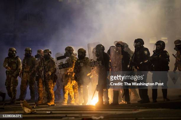 Federal officers and Portland riot police stand in the tear gas while clearing the streets early morning during protests on July 26, 2020 in...
